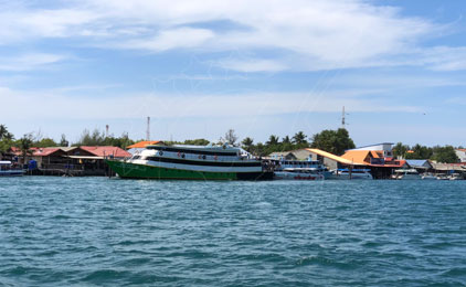 Ferry de passageiros colorido e barcos de madeira atracados num píer tropical com água turquesa