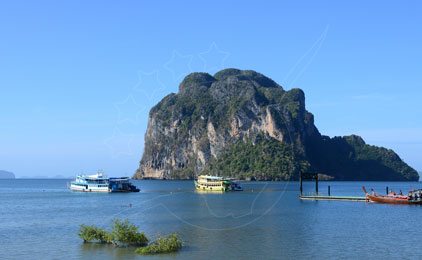 Ilha de karst calcário com barcos de pesca tradicionais e longtail atracados em águas turquesa calmas