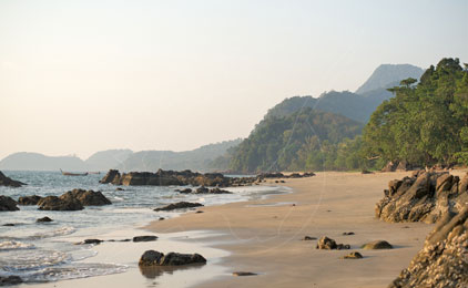 Praia tropical intocada com rochedos, águas turquesa calmas e encosta arborizada ao amanhecer