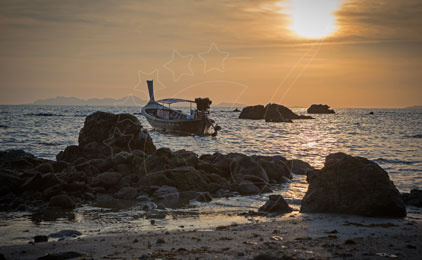 Barco de pesca de madeira desgastado ancorado entre rochas ao pôr do sol numa praia tropical