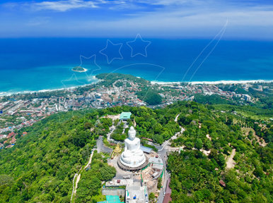 Vista aérea de uma grande estátua branca de Buda sentado num topo de colina arborizado sobre a costa de Phuket e o mar turquesa