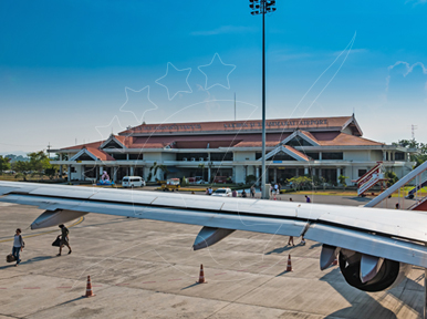 Terminal de aeroporto regional com telhados de telha em socalcos atrás da asa de um avião, enquanto passageiros atravessam a pista