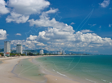 Ampla praia de areia curvando-se até hotéis altos ao longe sob nuvens cumulus imponentes, mar turquesa