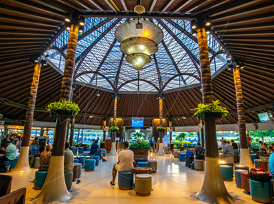 Terminal tropical ao ar livre com cúpula de treliça de madeira, colunas de troncos de palmeira e viajantes com bagagem