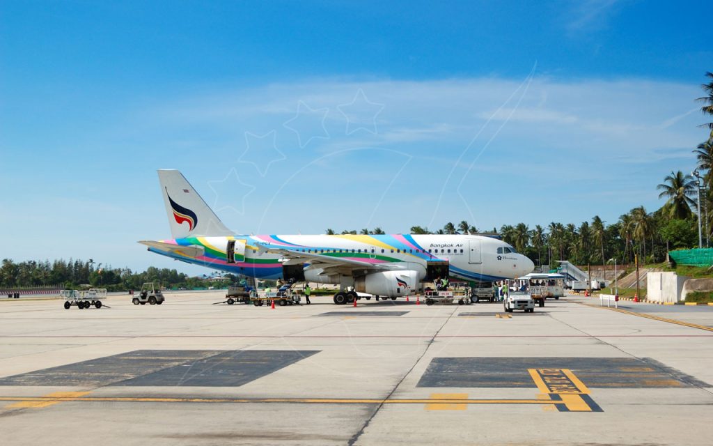 Airbus A319 da Bangkok Air estacionado na placa de um aeroporto tropical com palmeiras e pessoal de terra
