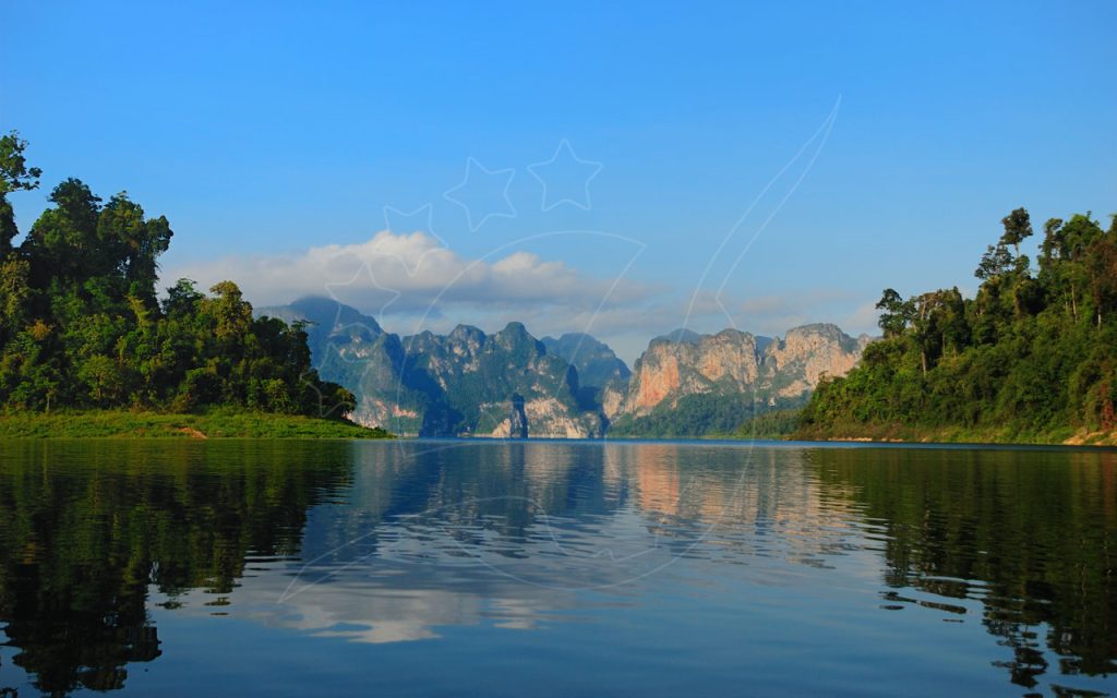 Calm emerald lake reflecting limestone karst cliffs and jungle-covered shores under a clear blue sky