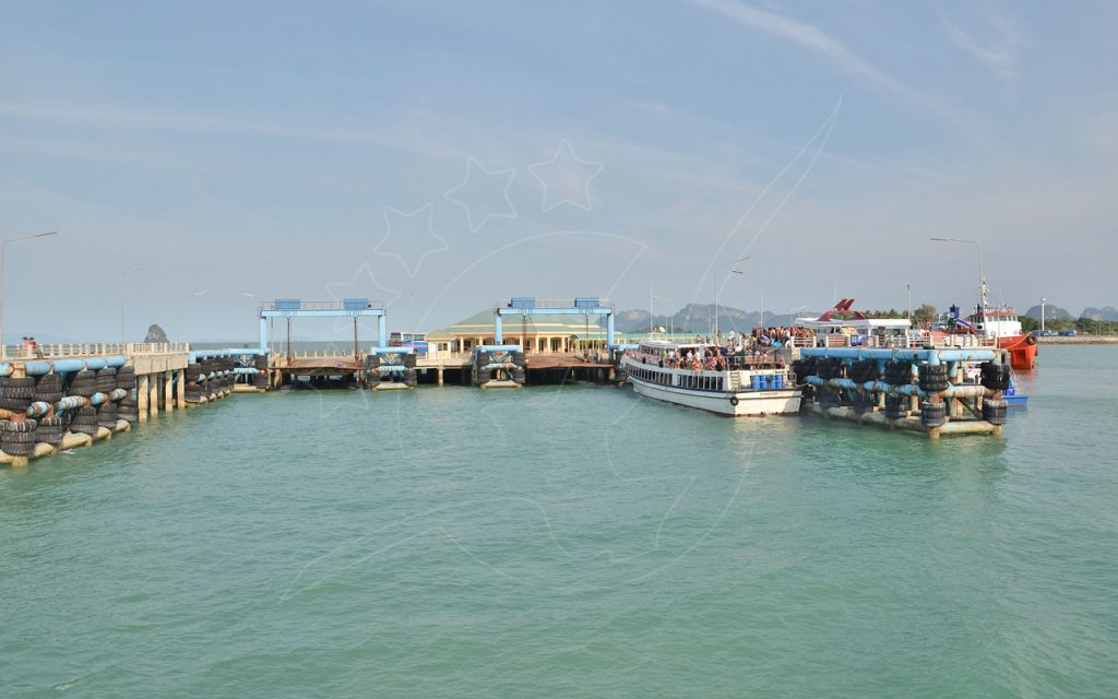Embarque num ferry de passageiros num cais de betão com defensas de pneus em mar turquesa calmo, colinas calcárias no horizonte