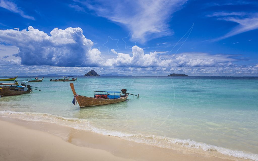 Barcos longtail de madeira atracados em águas turquesa transparentes ao largo de praia de areia branca, ilhas no horizonte