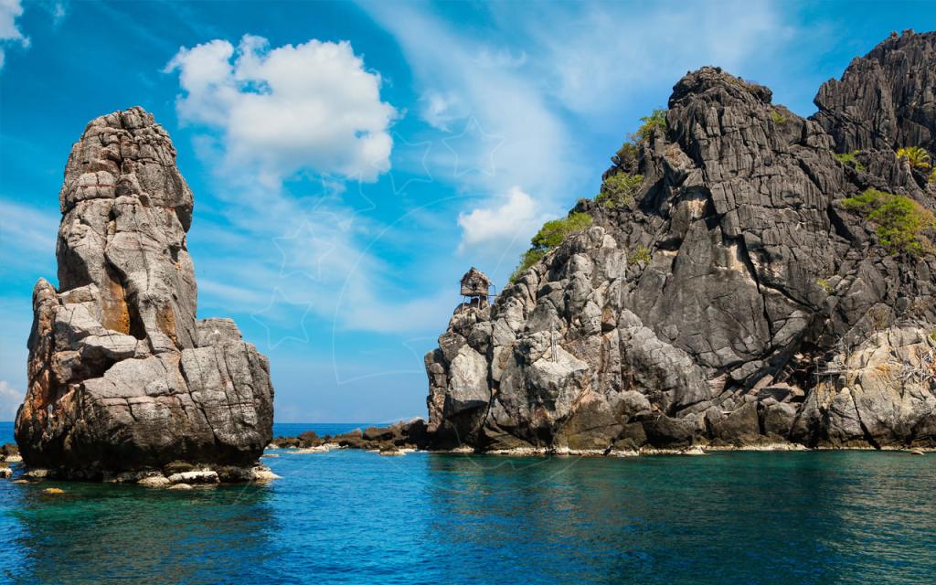 Alto rochedo de calcário e ilha rochosa acidentada com uma pequena cabana, erguendo-se da água turquesa sob céu azul