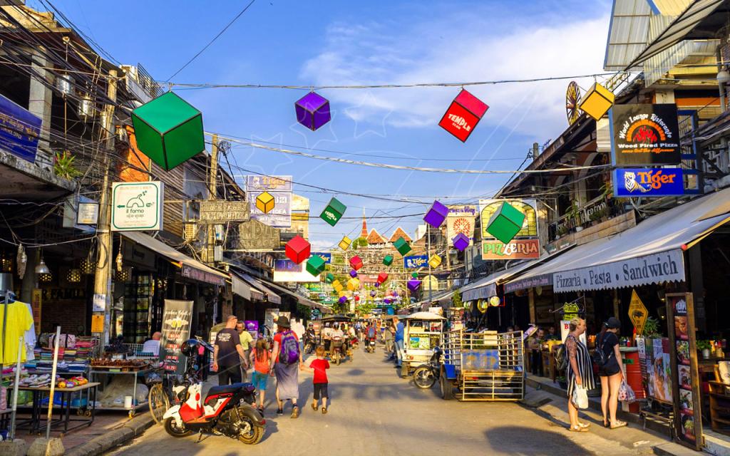 Pub Street em Siem Reap, Camboja, com lanternas coloridas, letreiros de bares, turistas e motos ao anoitecer