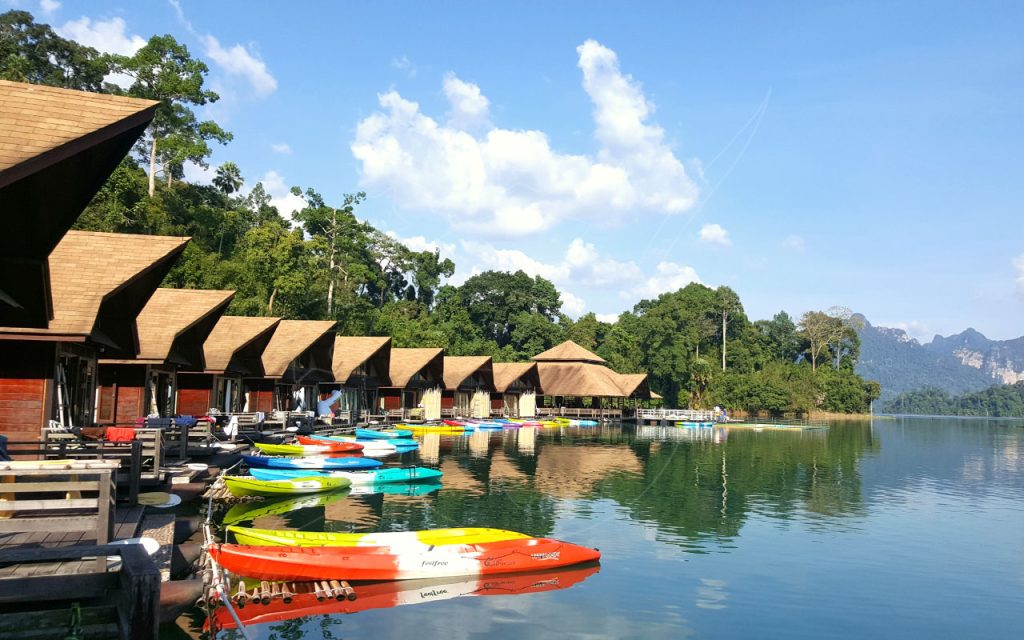 Bangalós flutuantes de colmo e filas de caiaques coloridos num lago calmo na selva, Tailândia