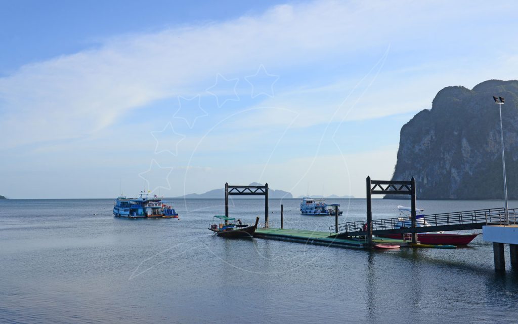 Cais flutuante com barco longtail e caiaques, ferries ancorados ao largo junto a promontório de calcário ao amanhecer