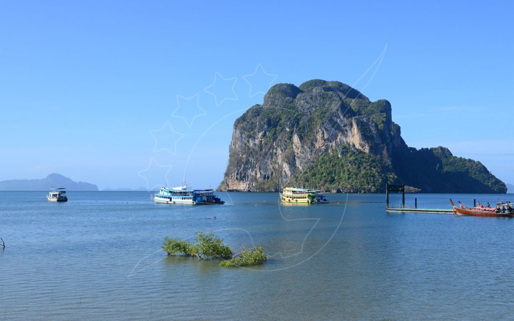 Ilha de calcário sobre mar azul calmo com ferries de passageiros, barcos longtail e um cais de betão