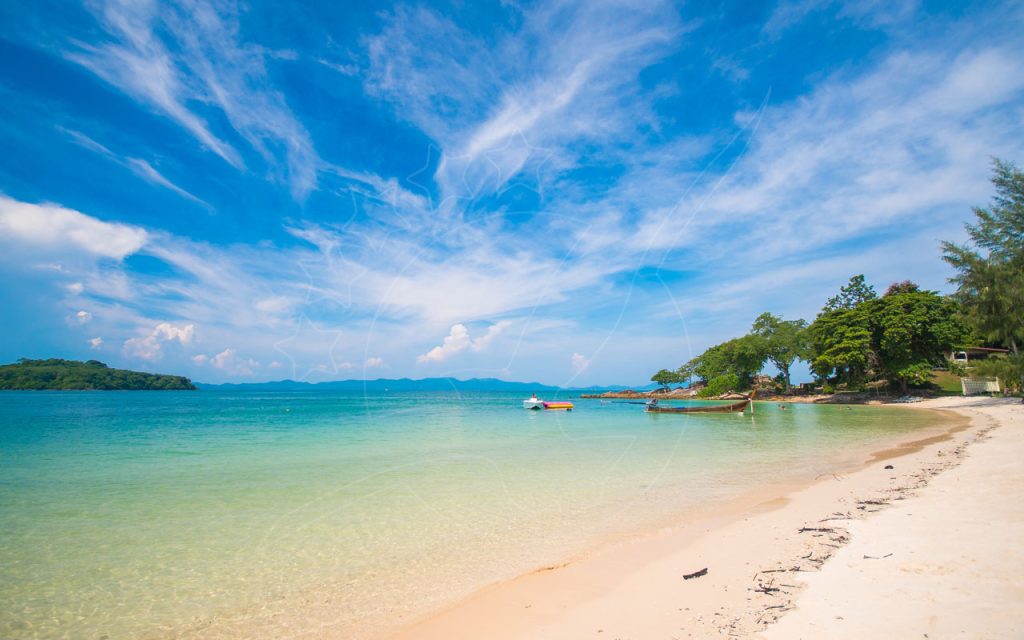 Praia de areia branca com águas turquesa cristalinas, barco longtail e lancha ancorados, promontório arborizado sob céu azul