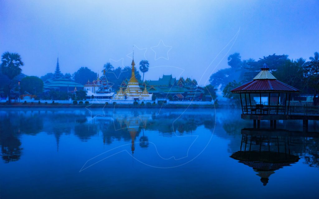 Templo e pavilhão tailandeses dourados refletidos num lago com névoa à hora azul, Mae Hong Son