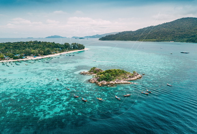 Vista aérea de uma ilhota rochosa rodeada de barcos longtail em águas turquesa de recife junto a uma praia arborizada