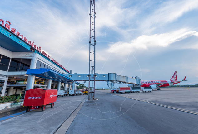 Avião da AirAsia estacionado no terminal do Aeroporto de Surat Thani com ponte de embarque e carros de bagagem vermelhos na placa
