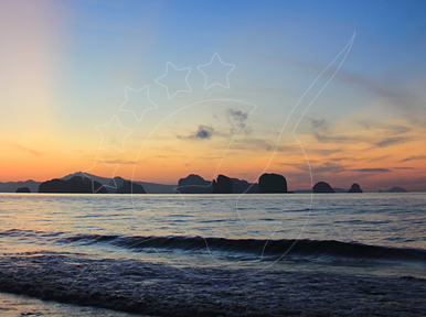 Pôr do sol sobre mar calmo com ilhas calcárias no horizonte e ondas suaves a quebrar numa praia de areia