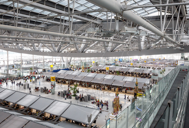 Vista elevada do átrio de check-in de um terminal aeroportuário moderno, com filas de balcões, teto de vidro e vigas de aço
