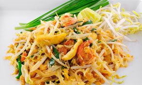 Noodles Pad Thai com camarão, ovo, rebentos de feijão frescos, cebolinho e uma rodela de lima num prato branco