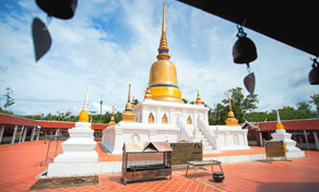Chedi branco de pináculo dourado num templo budista tailandês, pátio de telha laranja, sinos a enquadrar a vista