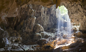 Luz do sol a entrar por uma abertura numa gruta calcária com formações rochosas e estalactites