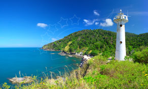 Farol branco num promontório verde sobre o mar turquesa, sob céu azul com nuvens dispersas