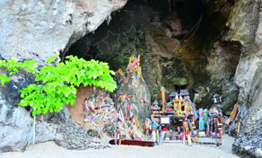 Santuário da fertilidade colorido com esculturas fálicas de madeira numa gruta calcária junto a praia e árvore verde