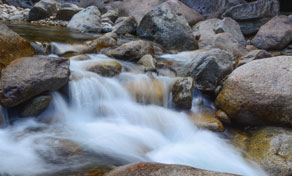 Long-exposure mountain stream flowing in silky white cascades over large grey and brown boulders