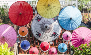 Sombrinhas de papel artesanais em vermelho, amarelo, azul e rosa expostas ao ar livre, uma pintada com elefantes