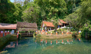 Piscina natural turquesa junto a edifícios de templo de telha vermelha e santuários rodeados de selva tropical densa