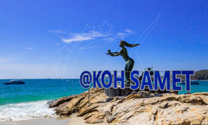 Estátua de bronze de sereia sobre rochas acima do mar turquesa na praia de Koh Samet, com barcos ao largo sob céu azul