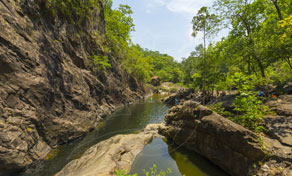 Garganta rochosa estreita com pedras escuras, árvores tropicais verdes e céu azul limpo