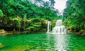 Cascata a cair de uma saliência rochosa para uma poça verde-esmeralda rodeada de selva tropical densa