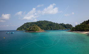 Promontório de ilha tropical arborizada com baía turquesa, barcos longtail ancorados e areal sob céu azul