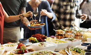 Convidados servem-se de uma mesa de buffet repleta de saladas, pães e pratos numa refeição informal com catering