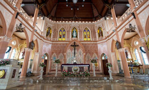 Interior de catedral em estilo gótico na Tailândia com colunas rosa-salmão, vitrais, altar florido e crucifixo