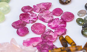 Turmalinas rosa esculpidas com cabochões de âmbar e verdes numa superfície branca, macro em close-up