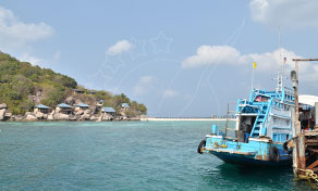 Ferry de passageiros azul e branco atracado num cais de betão junto a ilha tropical verde em água turquesa