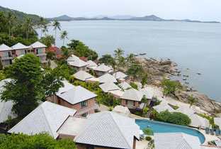 Resort costeiro com villas de telhados brancos, piscina e palmeiras sobre uma baía calma com ilhas distantes