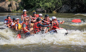 Grupo de capacete e salva-vidas remando bote inflável em corredeiras de um rio cercado de floresta