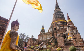 Antigo chedi de tijolo num templo tailandês com estátuas de Buda sentado em túnicas laranja e uma bandeira amarela