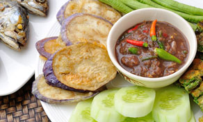 Nam prik tailandês numa tigela com cavala frita, fatias de beringela, pepino e feijão-verde longo num prato branco
