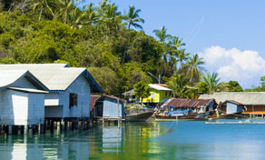 Palafitas e barcos longtail de madeira ao longo de aldeia de pescadores tropical com palmeiras e água turquesa