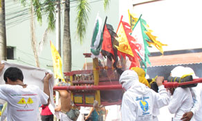 Devotos de branco carregam palanquim de santuário vermelho com bandeiras coloridas em procissão de rua tailandesa