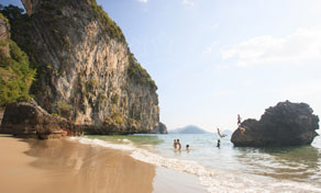 Praia tropical de areia com altas falésias cársticas de calcário e banhistas nas águas rasas turquesa