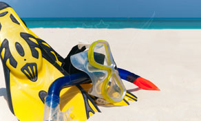 Barbatanas amarelas, máscara e tubo de snorkel na areia branca junto ao mar tropical turquesa