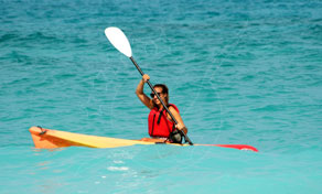 Pessoa de colete salva-vidas vermelho a remar um caiaque de mar amarelo em água turquesa brilhante