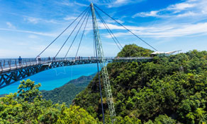 Passarela pedestre curva estaiada sobre floresta tropical densa com mar turquesa e ilhas ao fundo