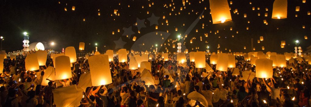 Milhares de lanternas de papel iluminadas a subir no céu noturno sobre multidões em festival